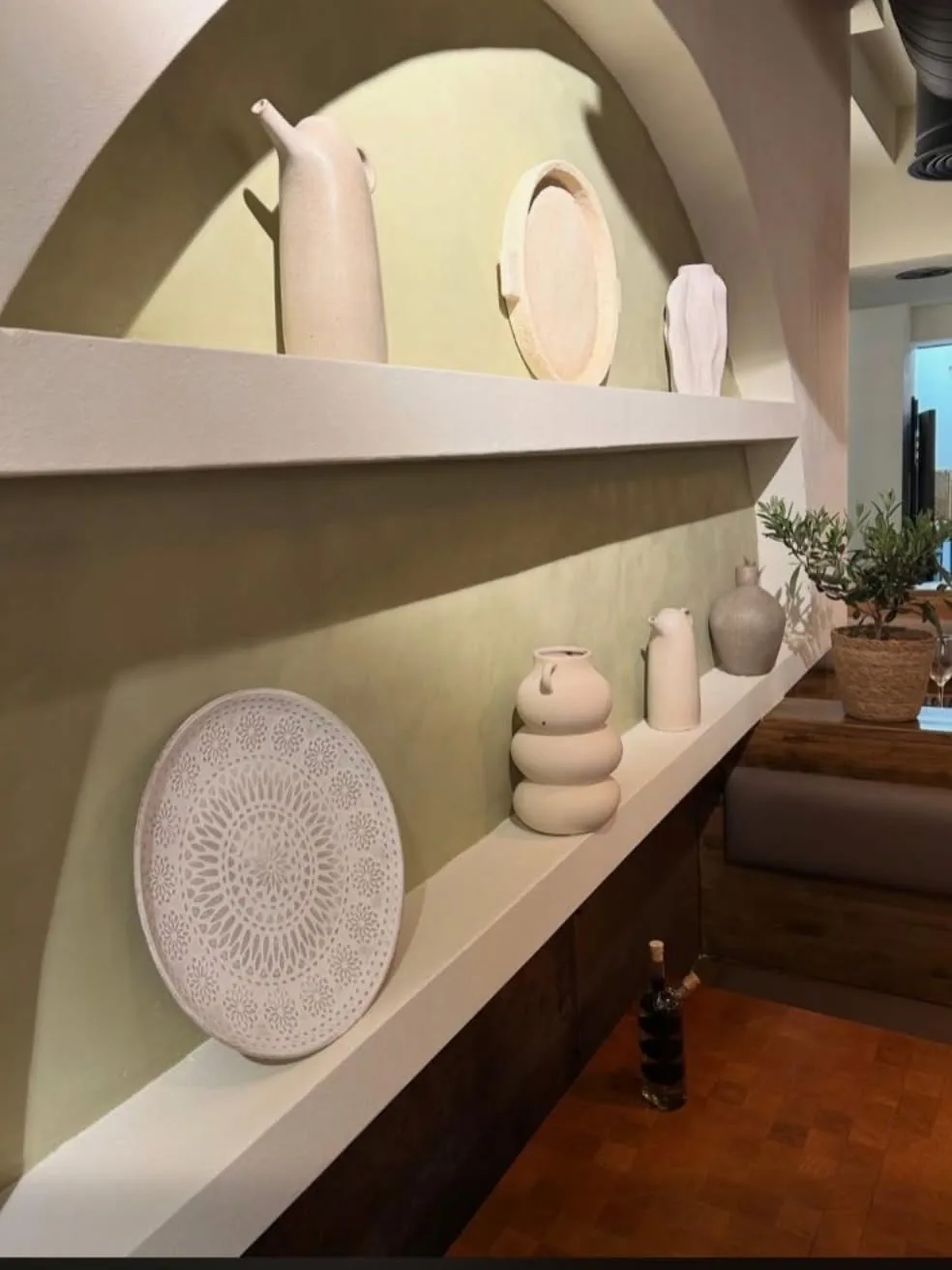 A sage-green arched alcove at Brizola displaying white Greek ceramic jugs and dishes