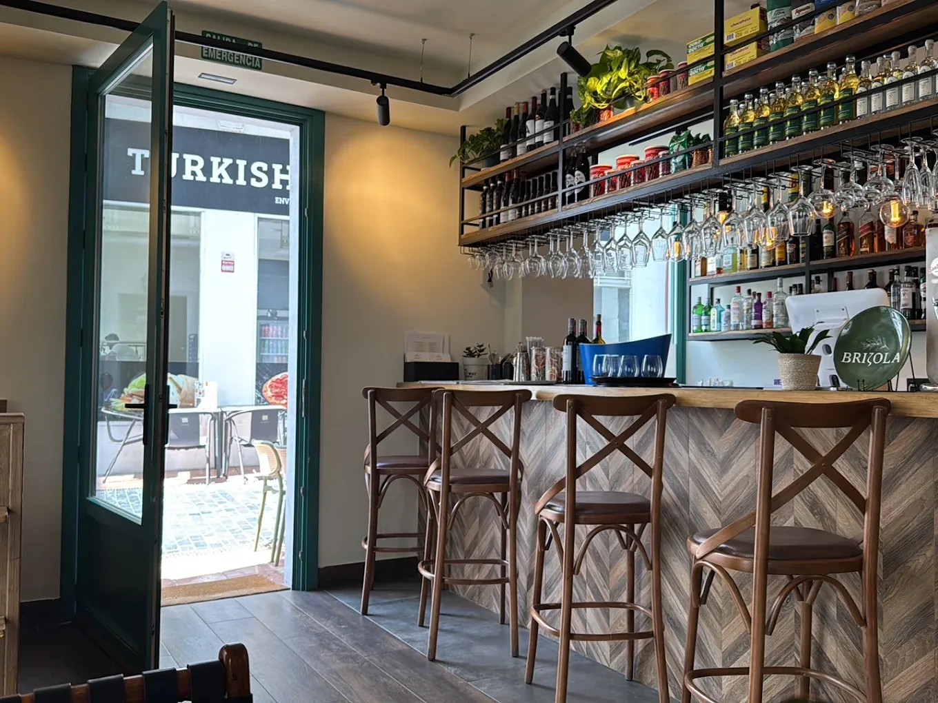 The Brizola bar — a herringbone timber counter, bentwood stools, hanging glassware and shelves of Greek spirits