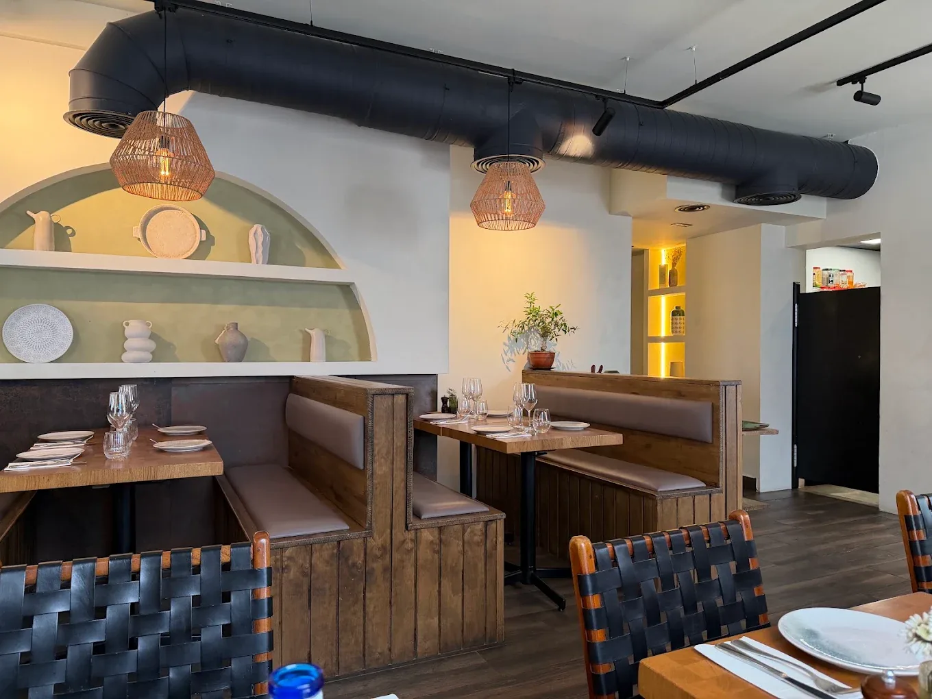 Wooden booths beneath a sage-green arched alcove set with white Greek ceramics