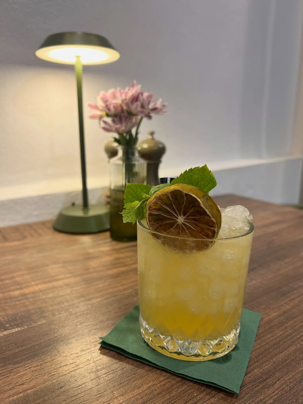 A citrus cocktail with mint and dried lemon on a Brizola table, lit by an olive-green lamp