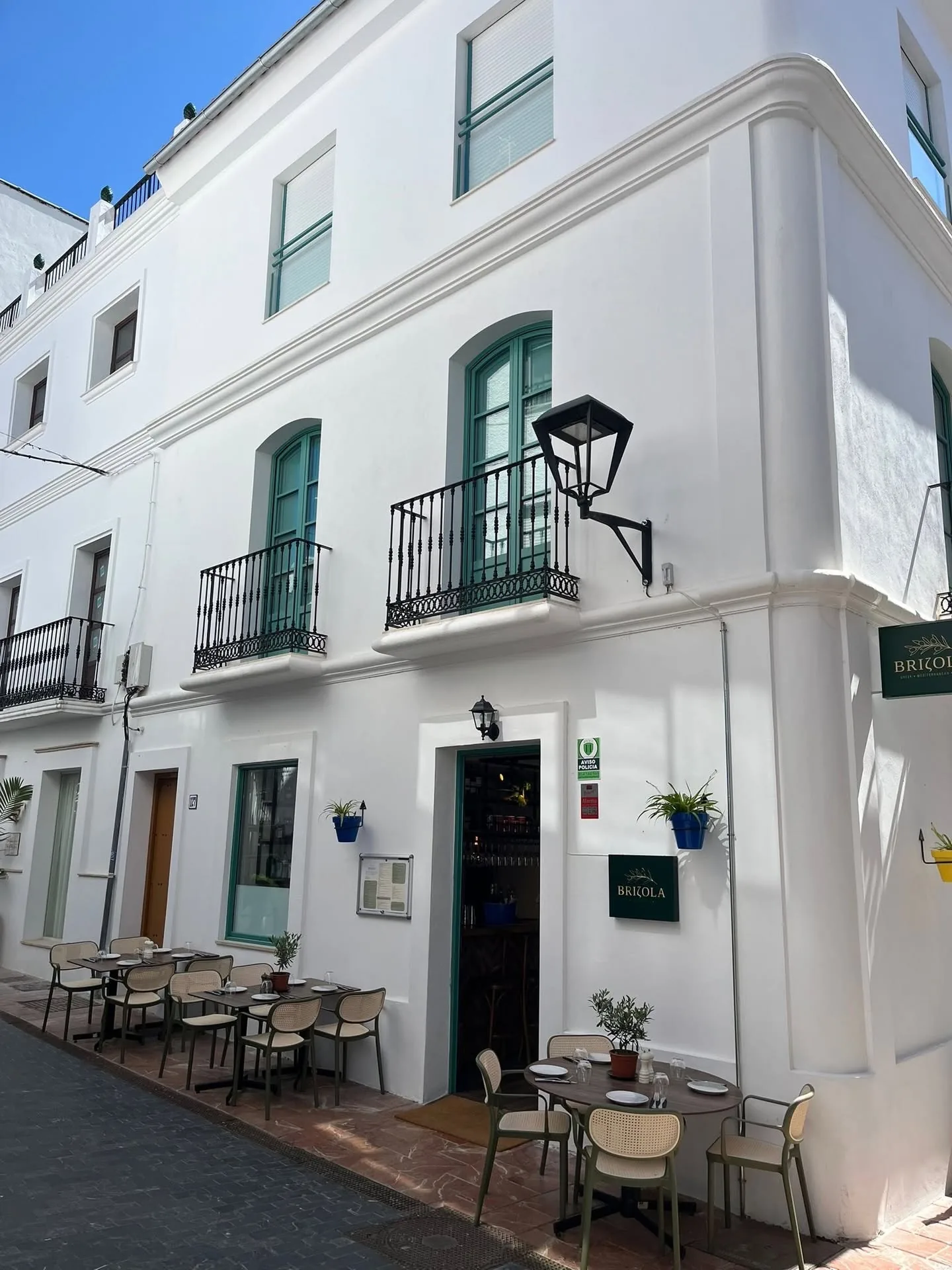 The whitewashed corner of the Brizola building in Estepona old town, with green shutters and terrace tables