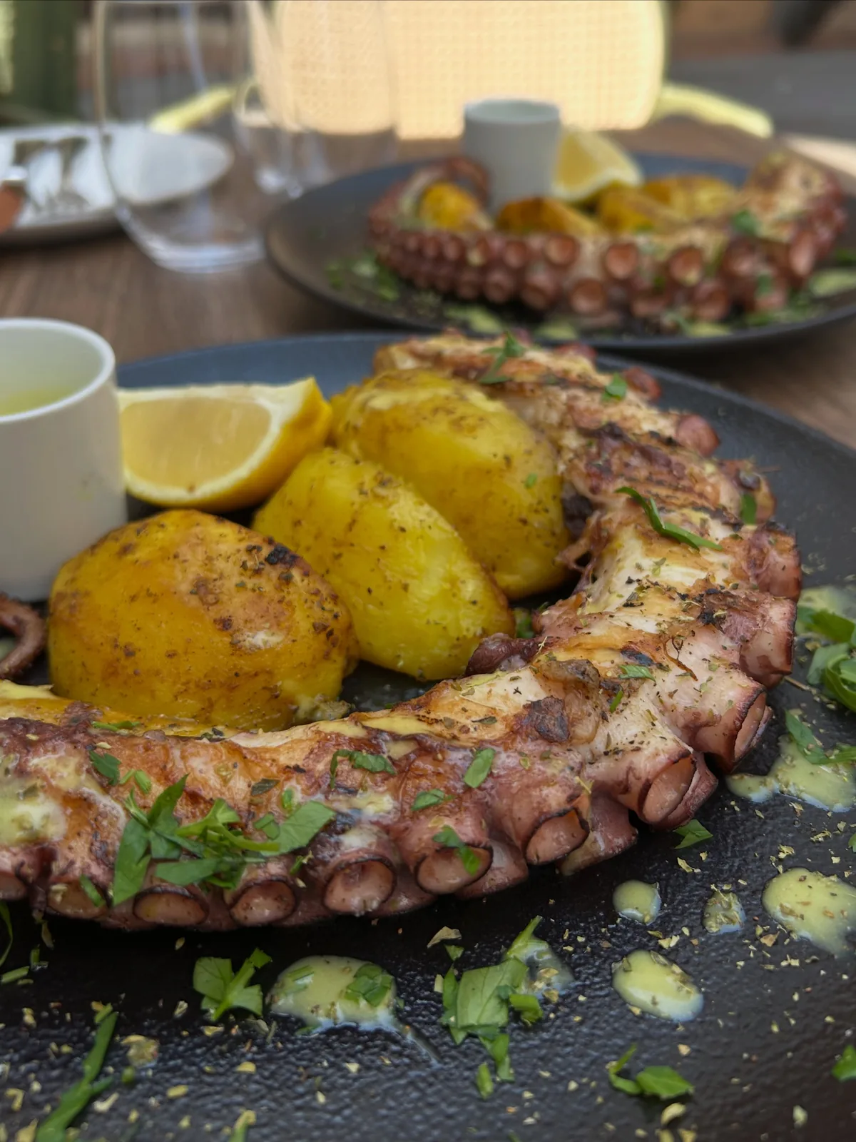 Grilled octopus with oven potatoes, lemon and herbs on a dark plate at Brizola