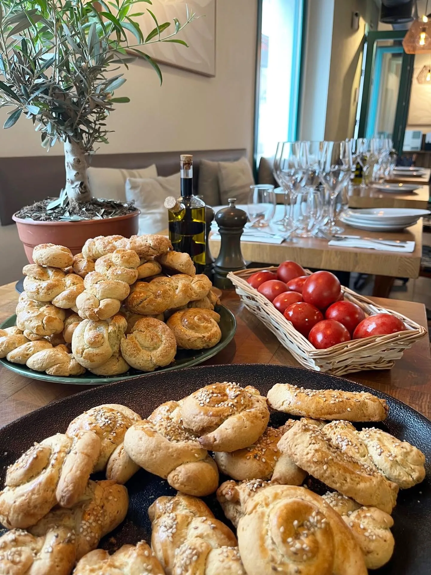 Trays of hand-twisted Greek koulourakia with sesame, beside a basket of eggs and an olive tree