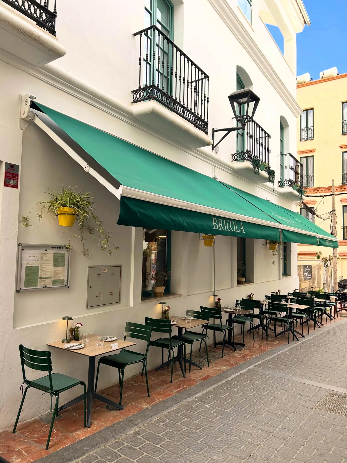 Brizola's terrace on Calle Caridad, Estepona — green awning, olive-green chairs and wooden tables against a whitewashed old-town facade